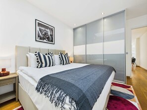 Un dormitorio moderno con una cama grande, almohadas a rayas, un plaid gris y una puerta corredera al armario.