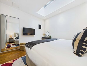 A modern bedroom with a large bed, a flat-screen TV, a mirror, and a skylight.