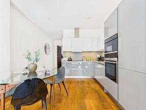 Una cocina moderna con una mesa de comedor de vidrio, sillas grises y electrodomésticos de acero inoxidable.