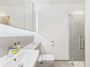 A modern bathroom with a large mirror, a white sink, a toilet, and a glass shower enclosure.