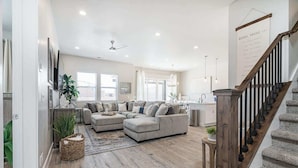 A spacious living room with a large sectional sofa, a wooden floor, and a staircase leading to the upper floor. - 52-53 | Family reunion home! 2 pools, 2 hot tubs (Santa Clara)