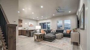 A spacious living room with a grey sectional sofa, a wooden coffee table, and a large window with blinds. - 52-53 | Family reunion home! 2 pools, 2 hot tubs (Santa Clara)