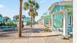 A beachfront hotel with outdoor seating, palm trees, and a clear sky. - Blessed Getaway Stay for 10! (Port Aransas)