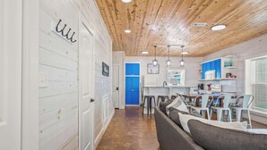 A modern kitchen with white cabinets, a blue door, and a dining area with a gray sofa and white chairs. - Blessed Getaway Stay for 10! (Port Aransas)