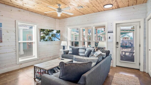 A cozy living room with a wooden ceiling, a ceiling fan, and a large window with blinds. - Blessed Getaway Stay for 10! (Port Aransas)