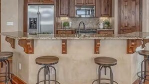 Une cuisine avec des meubles en bois, un réfrigérateur en acier inoxydable, un plan de travail en granit et des tabourets de bar.