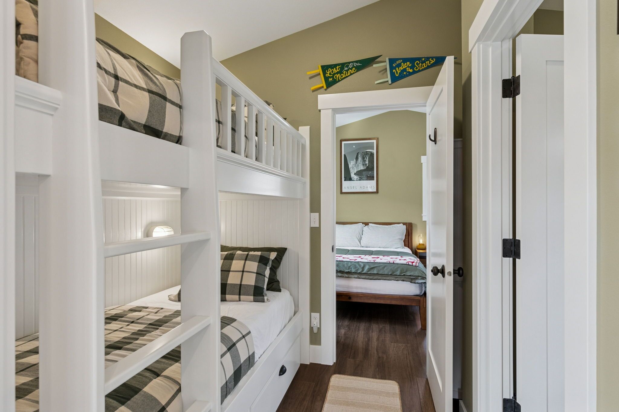 A bedroom with bunk beds, a door, a framed picture on the wall, and a small rug on the floor.