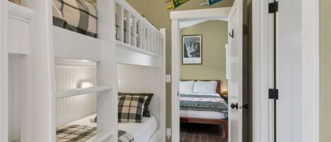 A bedroom with bunk beds, a door, a framed picture on the wall, and a small rug on the floor.