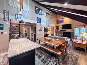 A spacious living area with a kitchen, dining table, and seating. A staircase leads to an upper level. - Spacious 4bd 2ba condo- near Sugar's Golf and Tennis (Sugar Mountain)