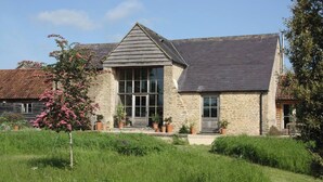 A stone building with a gabled roof, large windows, and a small porch with potted plants. - Spacious and beautifully converted 18th century stone barn.  Pet-friendly! (Lullington)