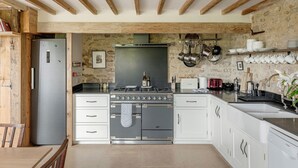 A kitchen with a built-in oven, a stove, and a sink. There is a wooden ceiling and stone walls. - Spacious and beautifully converted 18th century stone barn.  Pet-friendly! (Lullington)