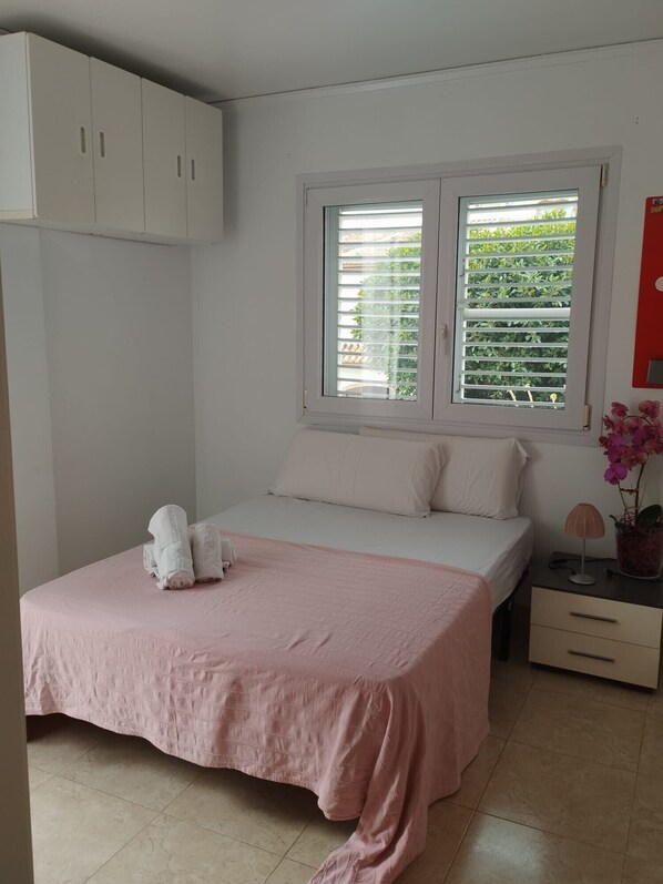 A bedroom with a bed, a nightstand, a window with blinds, and a wardrobe.