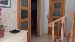 Un pasillo con una escalera, puertas de madera, un aparador blanco y un candelabro colgante.