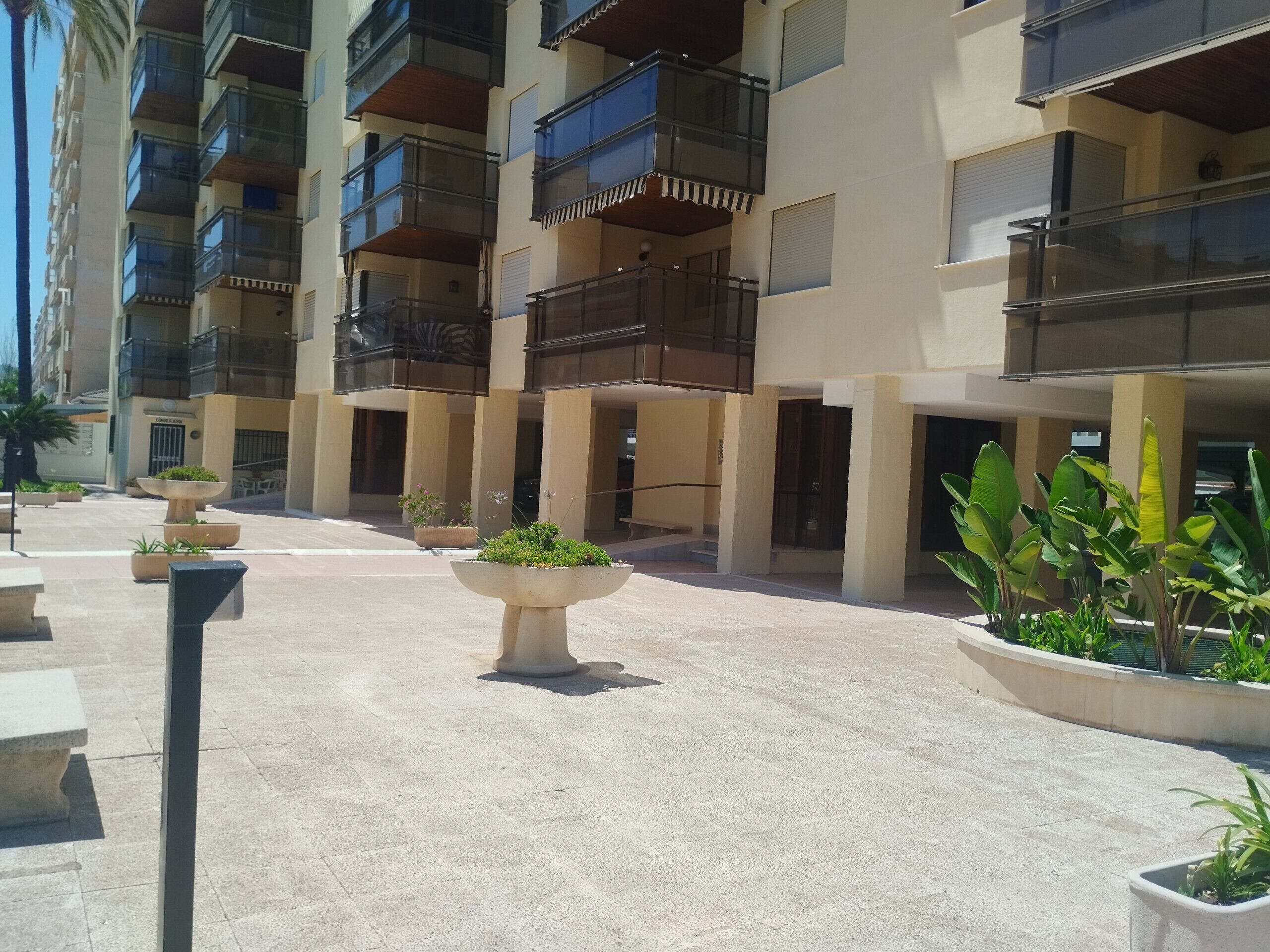 Un edificio moderno de varios pisos con balcones, macetas grandes y un patio empedrado.
