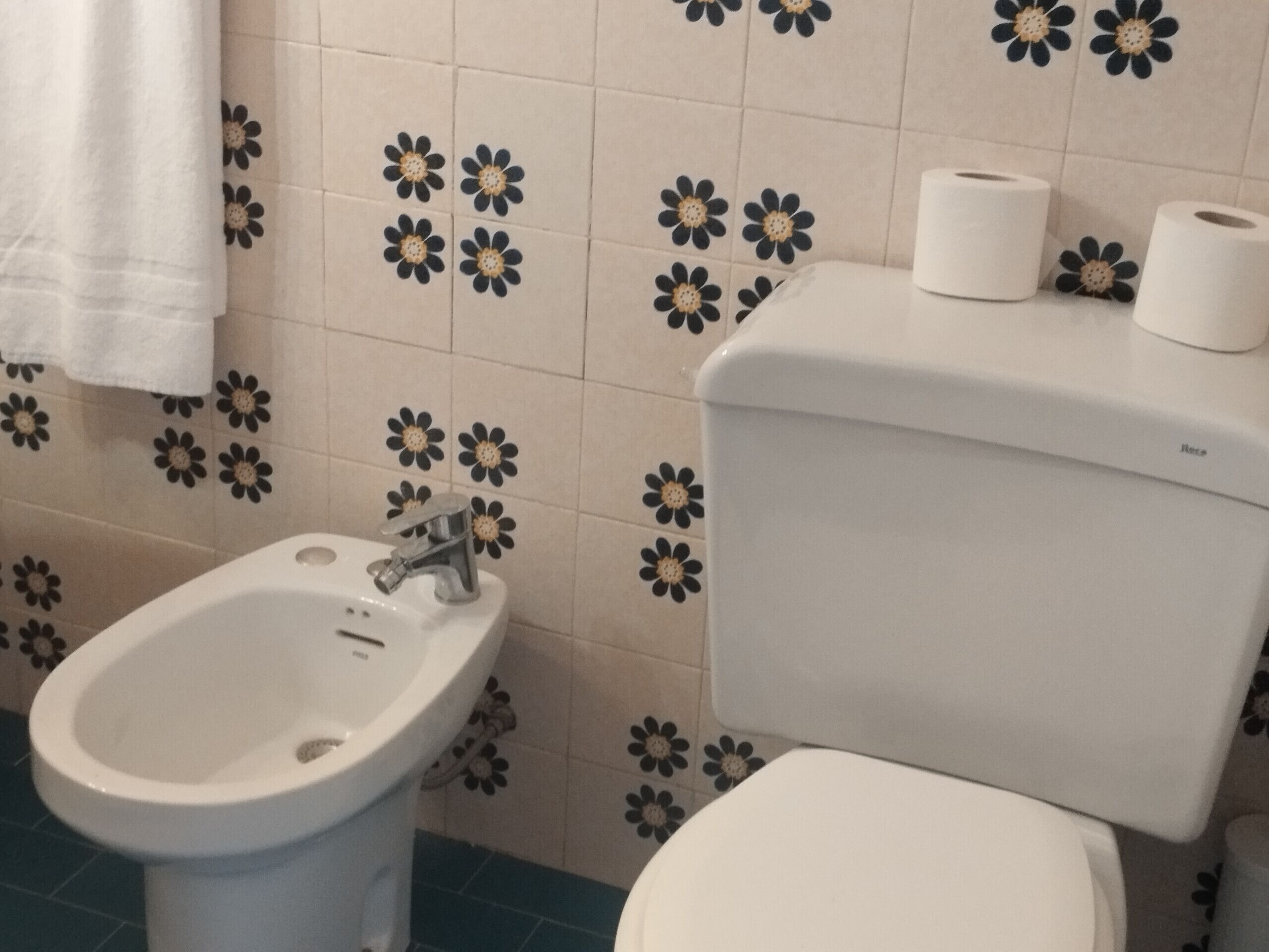 A bathroom with a bidet, toilet, and toilet paper.