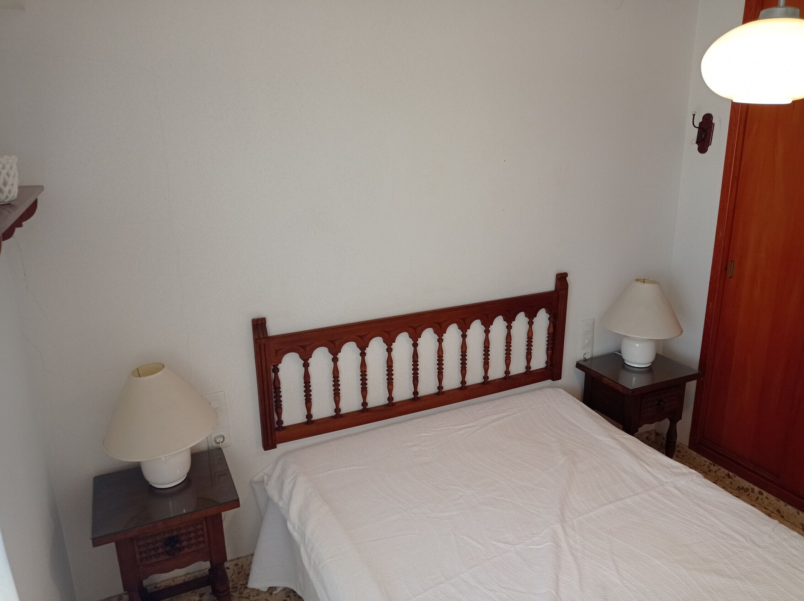 Une chambre à coucher avec une tête de lit en bois, un couvre-lit blanc, deux tables de chevet avec des lampes et une armoire en bois.