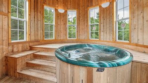 Un spa de madera con bañera de hidromasaje, ventanas amplias y escalones de madera.