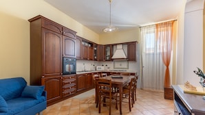 Una cocina con armarios de madera, una mesa de comedor con sillas, un sofá azul y piso de baldosas.