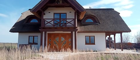 A two-story house with a thatched roof, a wooden balcony, and a large wooden door.
