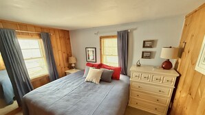 Ein Schlafzimmer mit einem Bett, einer Kommode, einem Nachttisch und einem Fenster mit Vorhängen.
