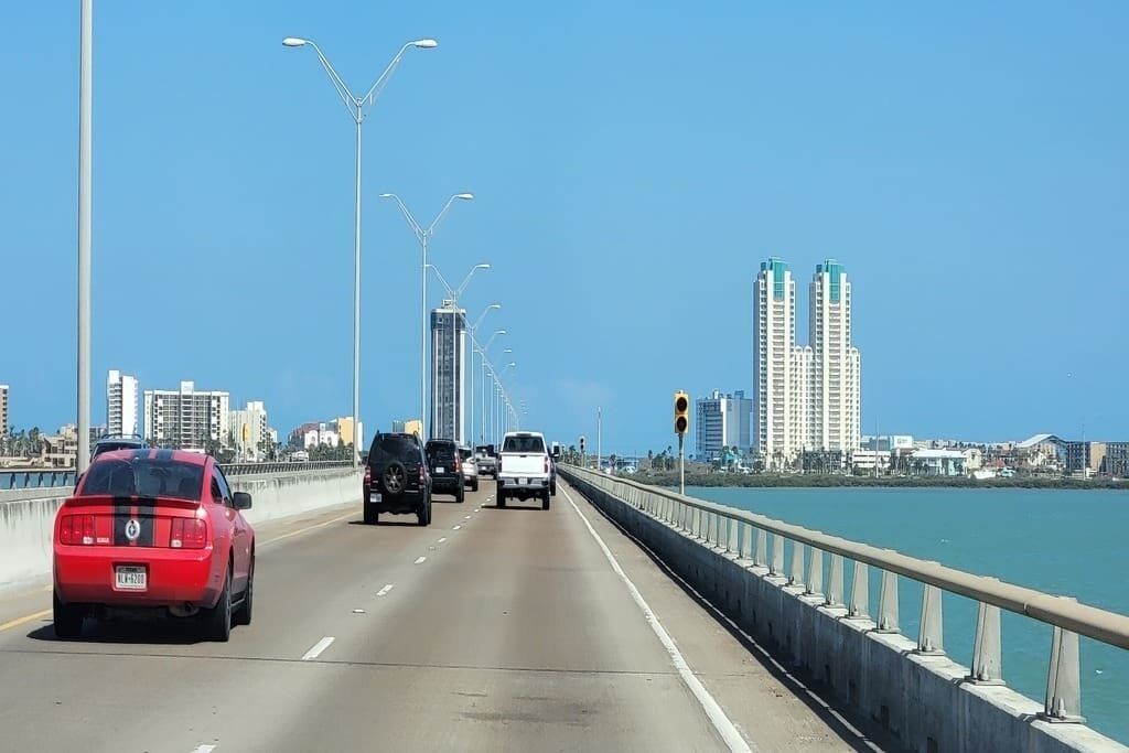 A multi-lane bridge with vehicles, a clear sky, and tall buildings in the background.