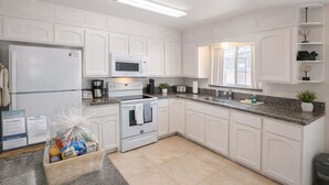 A modern kitchen with white cabinetry, a built-in microwave, a stove, and a sink. There are signs on the counter and a basket of groceries. - Campeche Retreat #12 2 Bedroom Condo (South Padre Island)