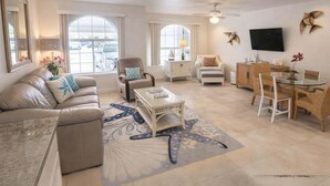 A spacious living room with a sofa, armchairs, a coffee table, and a dining area with chairs and a table. - Campeche Retreat #12 2 Bedroom Condo (South Padre Island)