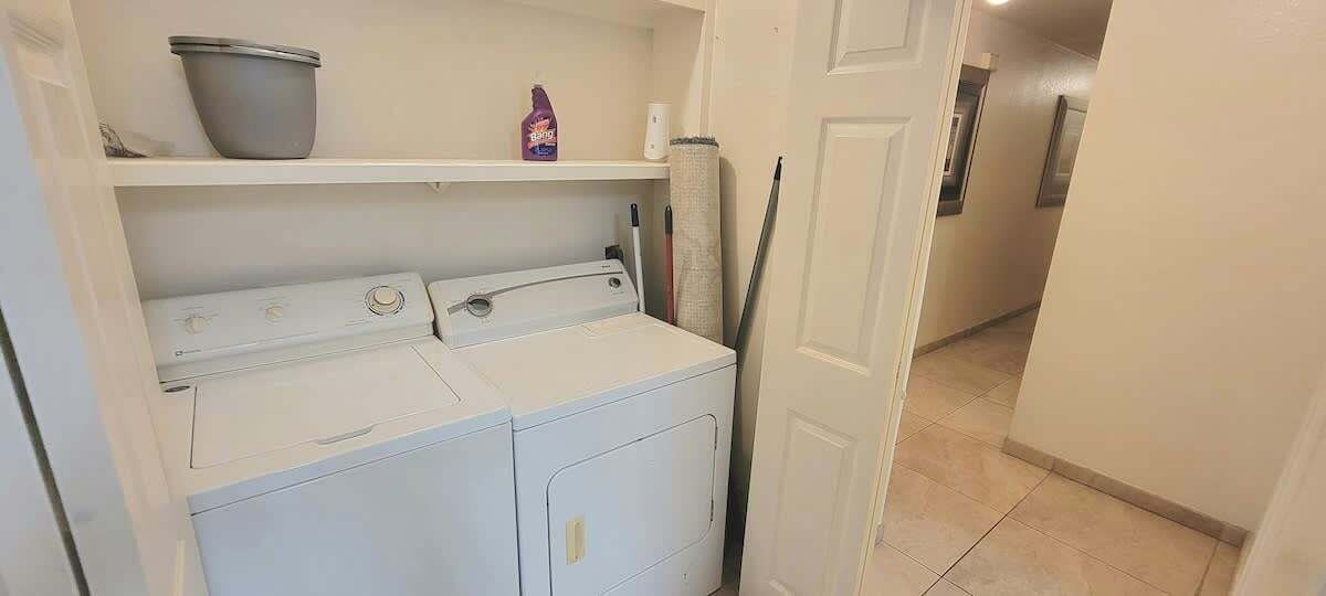 A laundry area with a washing machine and dryer, a shelf with a bucket, and a mop.