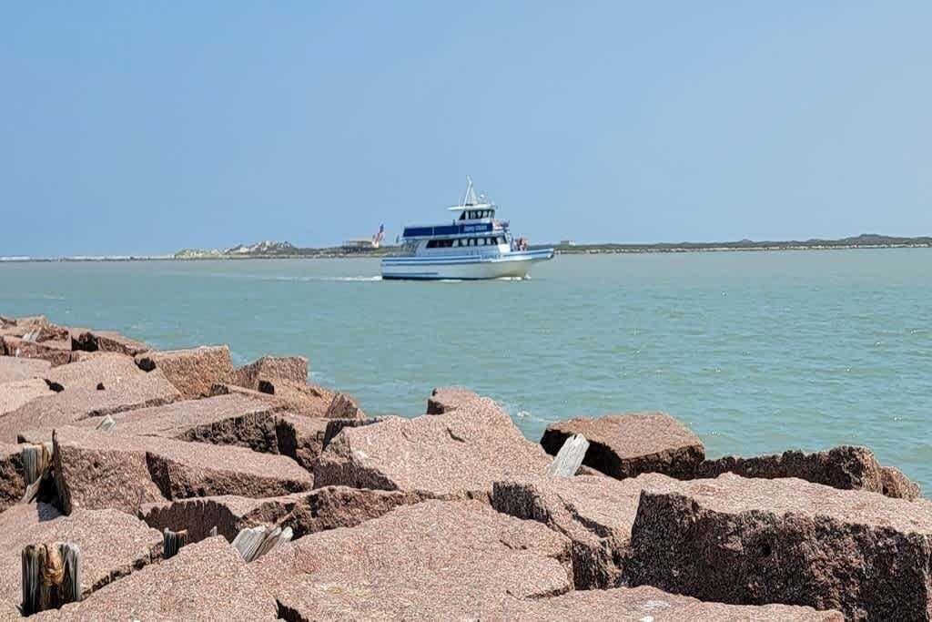 Un bateau sur une eau calme, une digue rocheuse et, au loin, une terre ferme parsemée de bâtiments.