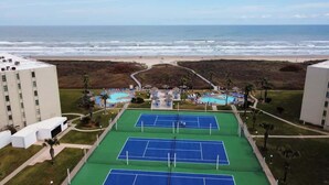 Un complesso di campi da tennis con vista sulla spiaggia, circondato da edifici.