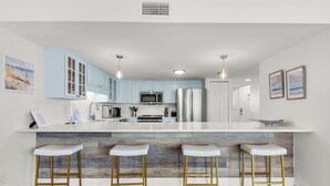 A modern kitchen with light blue cabinets, a white island with stools, stainless steel appliances, and wooden flooring. - 🌟Starboard Village 121: Beachfront Corner Unit w/ 2 Balconies🌟 (Pensacola Beach)