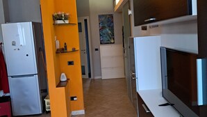 A modern kitchen with a wooden ceiling, a white refrigerator, a built-in oven, and a large flat-screen TV. - Home Ross. (Fiorenzuola d'Arda)
