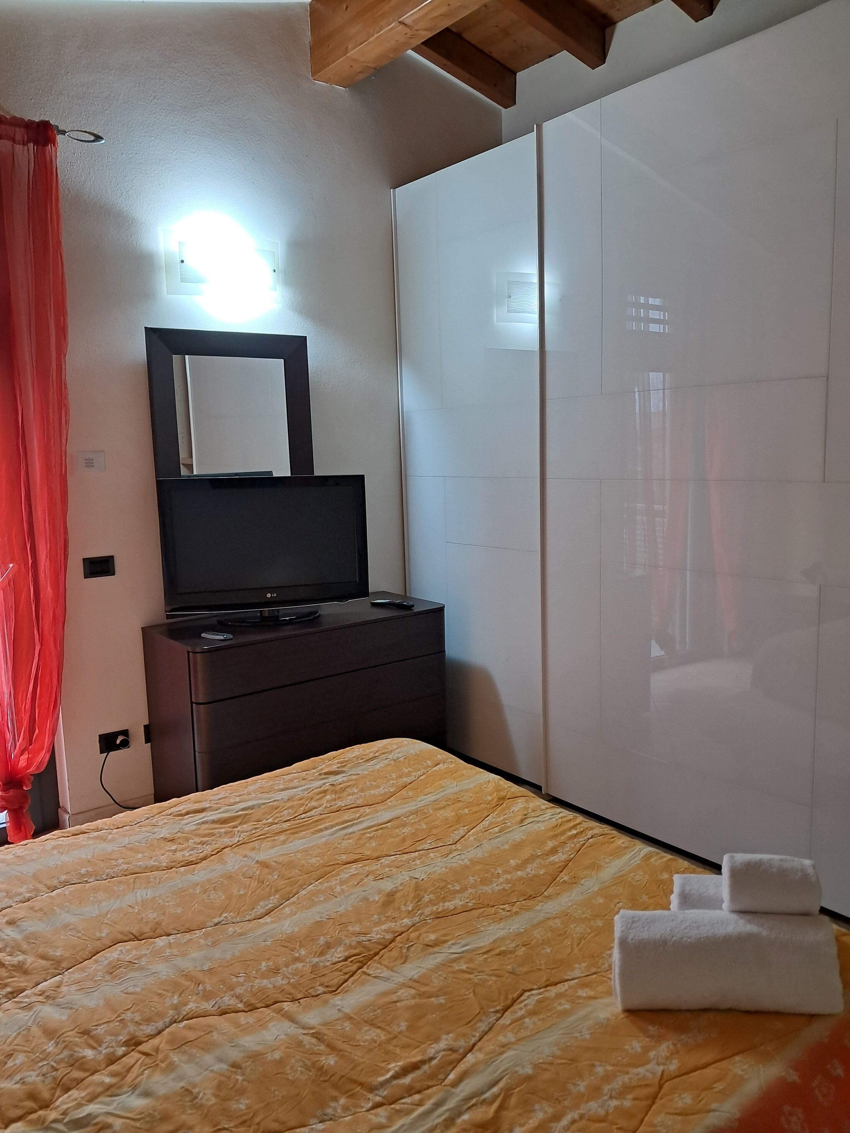 A bedroom with a bed, a TV on a dresser, a wardrobe, and a mirror on the wall.
