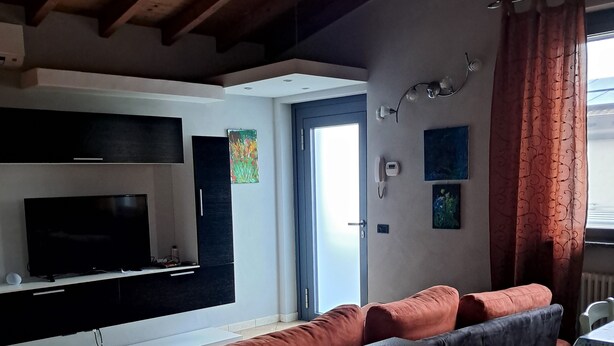 A modern living room with a flat-screen TV, a sofa, a dining table, and a kitchen area. - Home Ross. (Fiorenzuola d'Arda)
