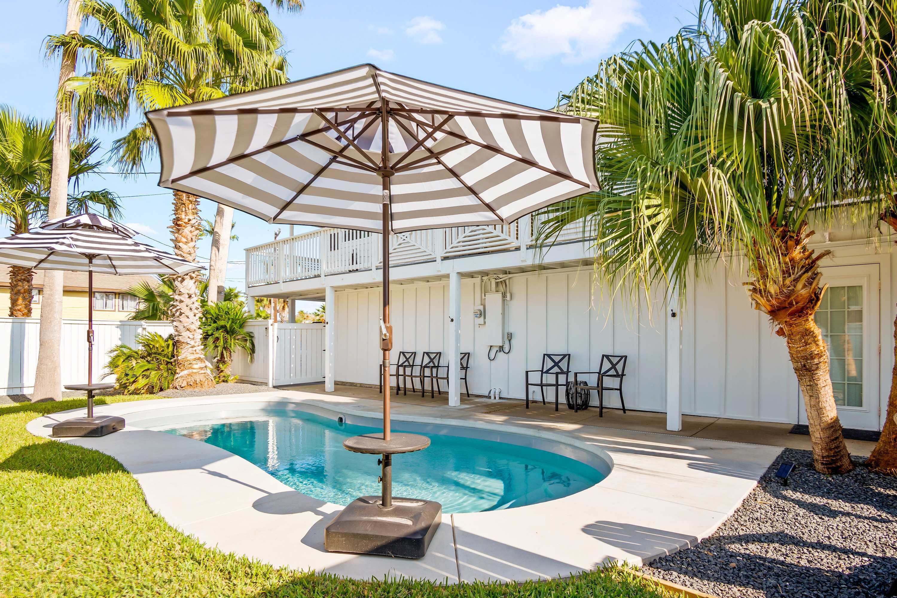 Une piscine de forme circulaire, entourée d’une terrasse blanche, de palmiers et de mobilier d’extérieur.