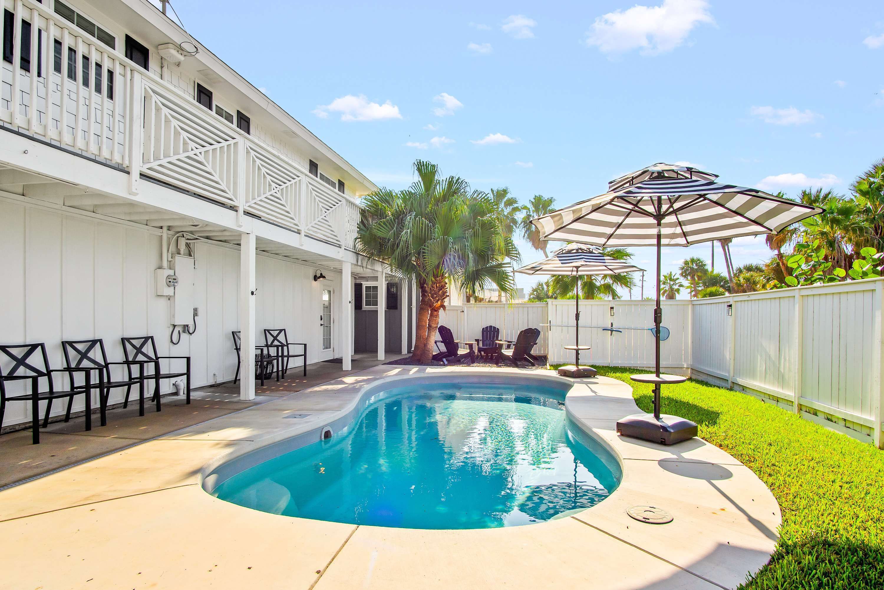 A backyard with a swimming pool, outdoor furniture, and a white fence.