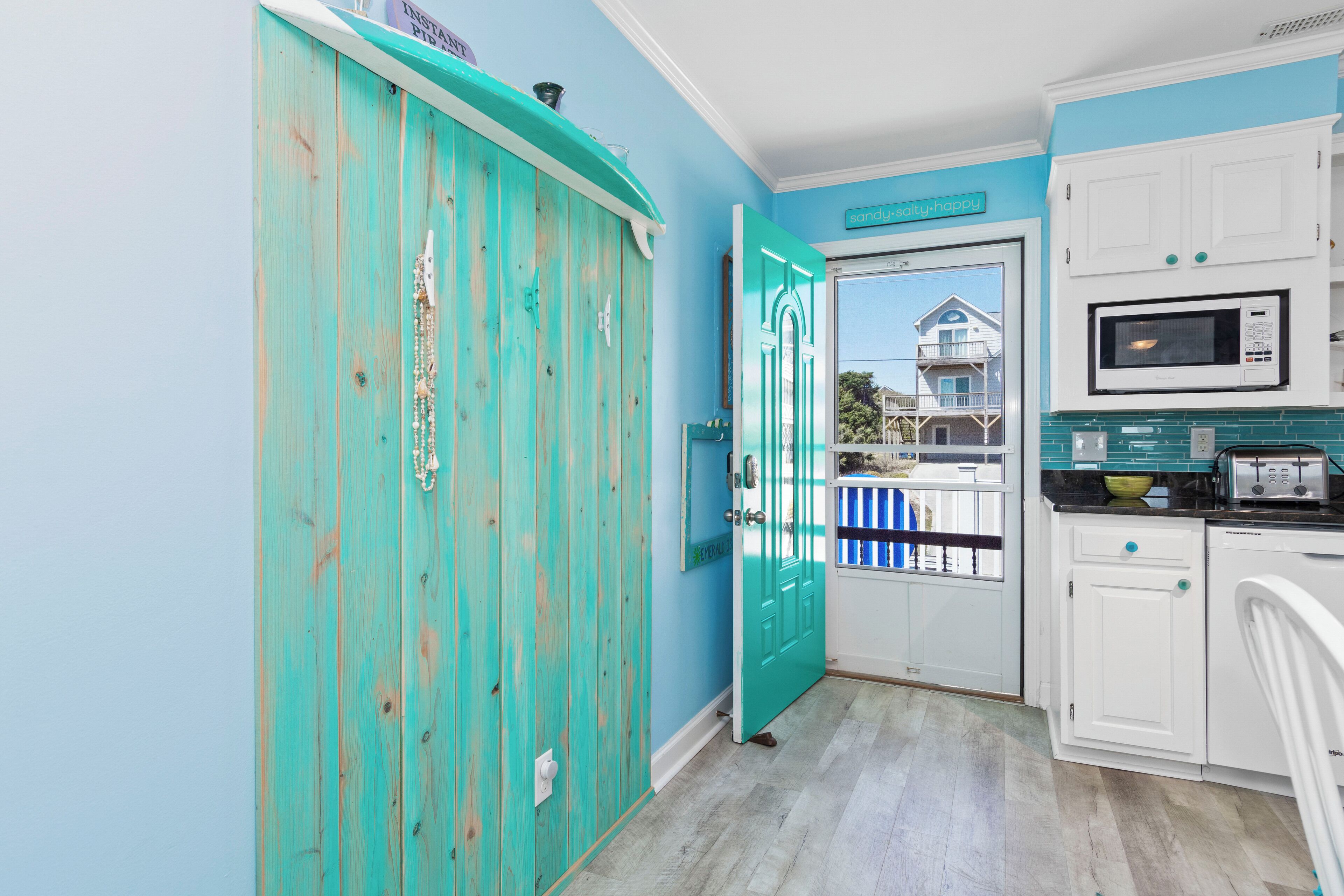 A kitchen with teal cabinetry, a white microwave, and a view of a balcony with a house.