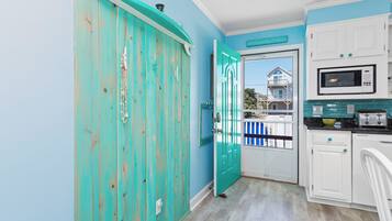 A kitchen with teal cabinetry, a white microwave, and a view of a balcony with a house.