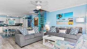 A modern living room with two grey sofas, a coffee table, and a staircase with teal railings.