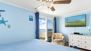 A bedroom with a bed, a chair, a dresser, a television, and a balcony with a view of the ocean. - Shady Shack West a 3 BR Oceanfront Duplex with Unobstructed Ocean Views (Emerald Isle)