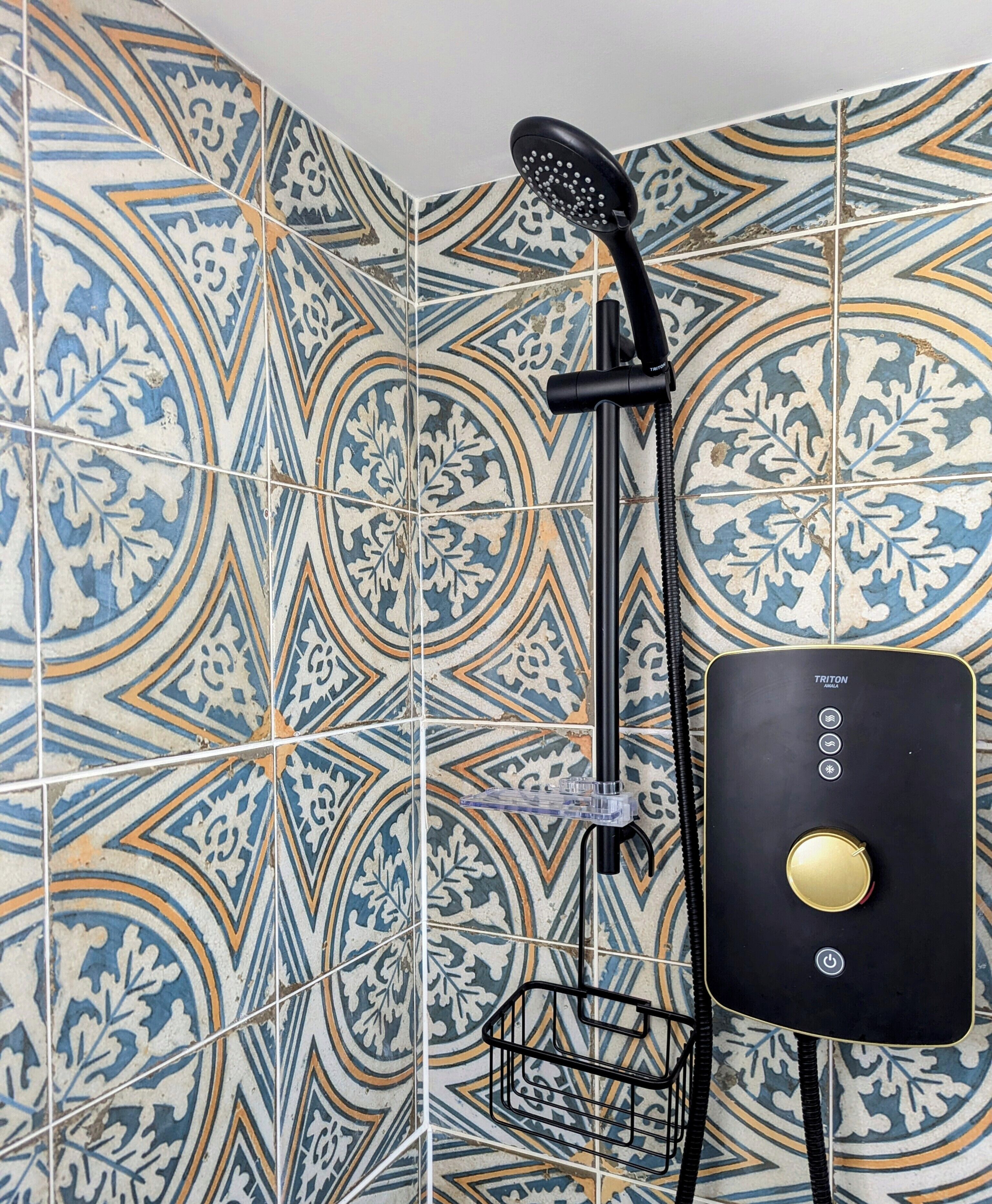 Un baño con baldosas estampadas, un cabezal de ducha y un panel de control negro.