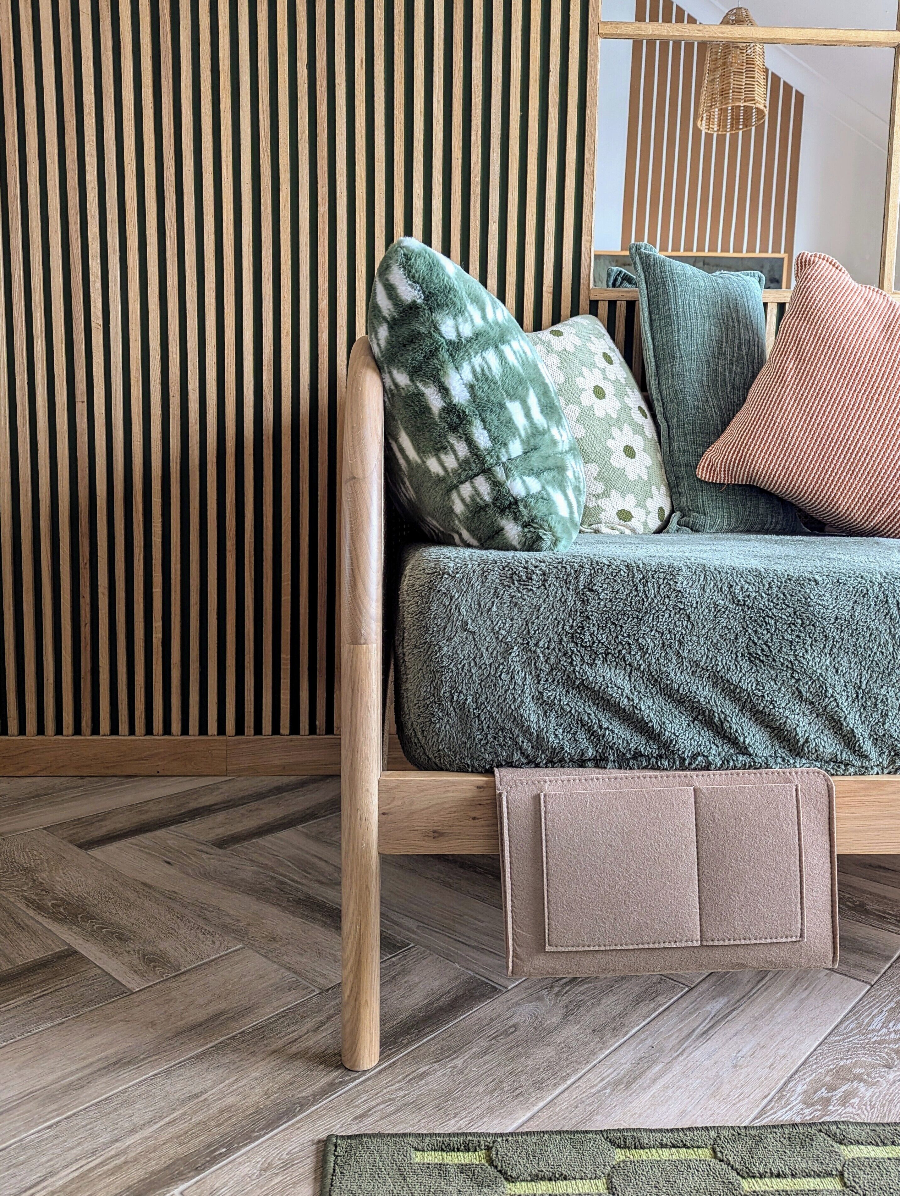 A wooden-framed sofa with a green patterned cover, multiple cushions, and a brown leather side table.