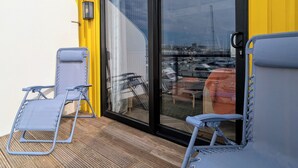 Une terrasse dotée de deux chaises longues bleues et d’une porte vitrée donnant sur une vue sur la marina.