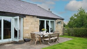 A stone building with a tiled roof, a patio with a table and chairs, and a grassy area. - The Mill set in stunning rural Northumberland (Netherton)