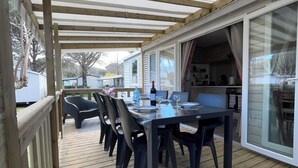 A covered outdoor dining area with a wooden deck, a table set for four, and chairs.