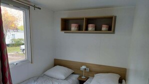 A room with two single beds, a wooden headboard, a bedside table with a lamp, and a shelf with three containers.