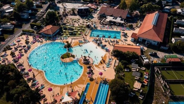 An aerial view of a resort with a large central pool, multiple smaller pools, and a variety of amenities including sun loungers and a water slide.
