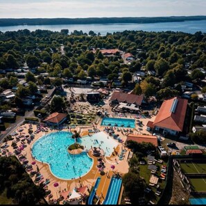 Une vue aérienne d’un complexe hôtelier doté d’une grande piscine centrale, de plusieurs piscines plus petites et de nombreuses installations, notamment des chaises longues et un toboggan aquatique.