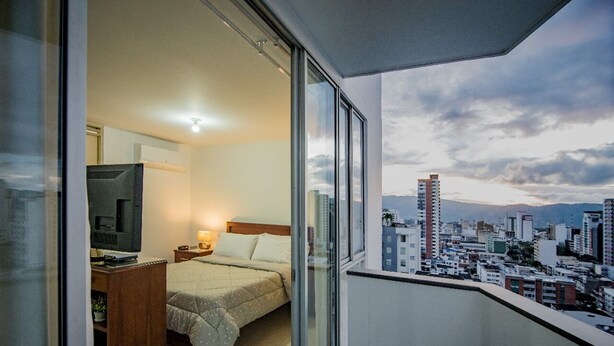 A hotel room with a bed, a TV, and a balcony with a city view. - Attractive apartment, well located, bright, comfortable, very complete, ventilated. (Bucaramanga)