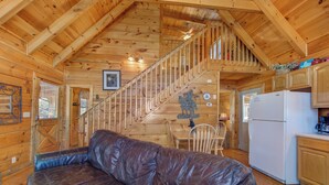 A wooden cabin interior with a leather couch, a staircase, a dining area, and a kitchen.